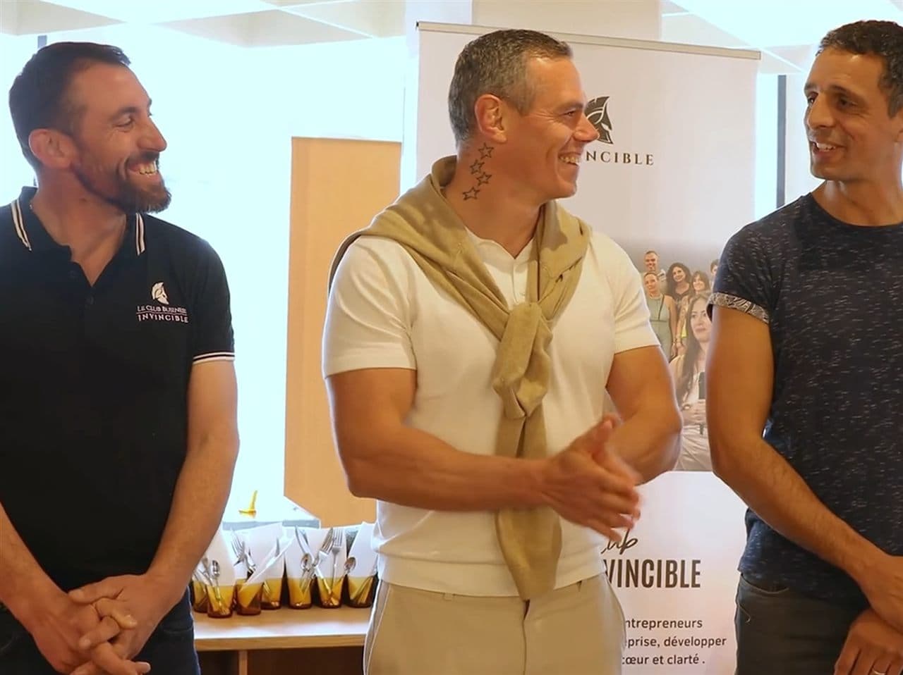 Trois membres du Club Business Invincible rient ensemble lors d'un petit-déjeuner du club, devant le kakémono Invincible